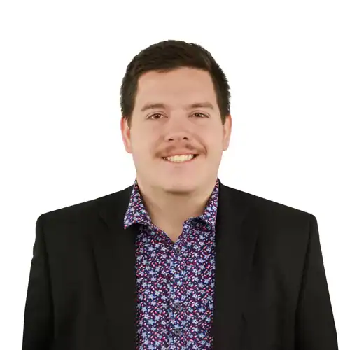 Headshot of a man with a mustache wearing a black suit and a patterned shirt.