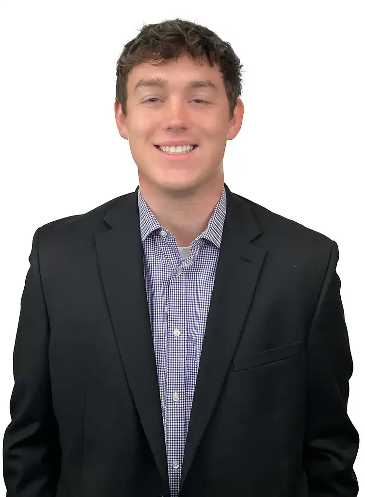 Logan O'Brien in a black suit and checkered shirt, smiling against a white background.