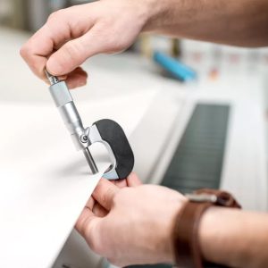 Person using a micrometer to measure the thickness of a paper sheet in a printing facility.