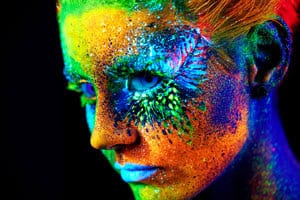 Close-up of a face adorned with vibrant neon body paint in various colors.
