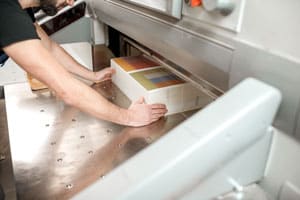 A person operating a paper cutting machine with a stack of printed paper.
