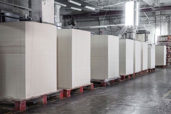 Stacks of unprinted paper on pallets in a warehouse setting.