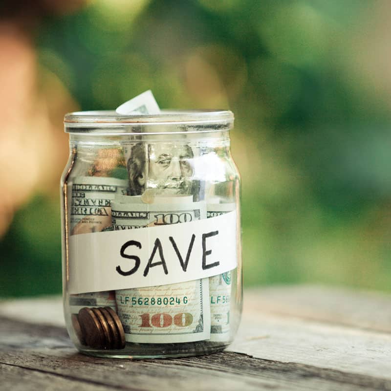 A glass jar filled with various denominations of currency and a label that reads 'SAVE'.