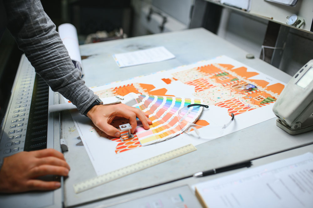 Printing Partners press operator inspecting color quality on a press sheet with a magnifying loupe