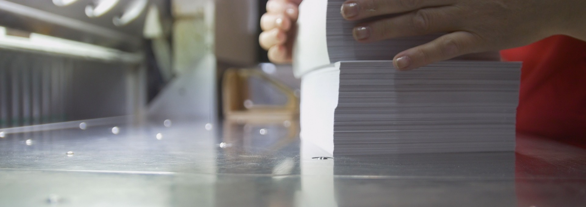 Printed cardstock sheets being lifted onto a guillotine cutter in a print shop