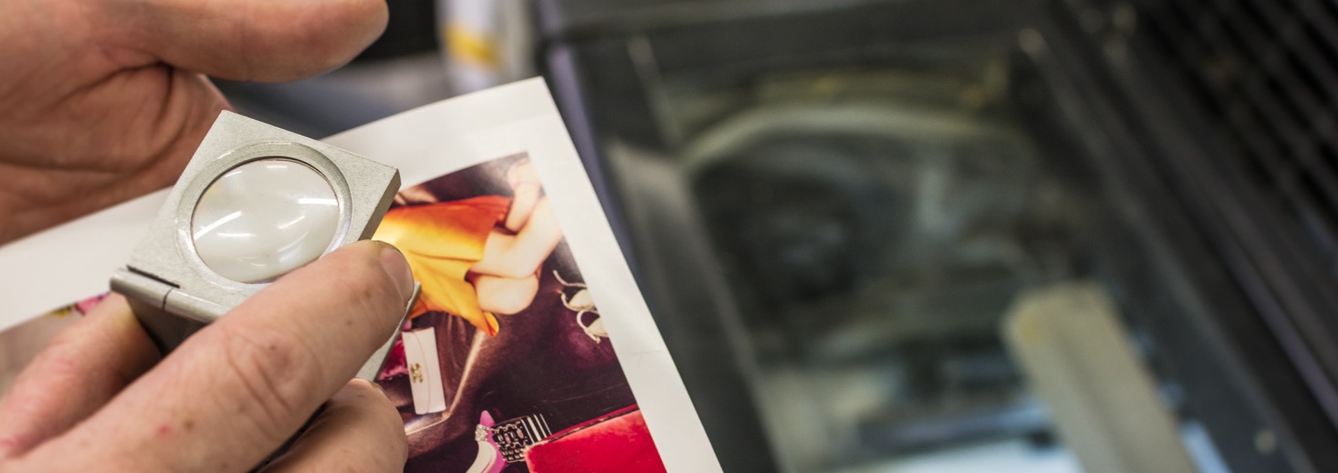 Press operator checking color on a printed sheet with a loupe